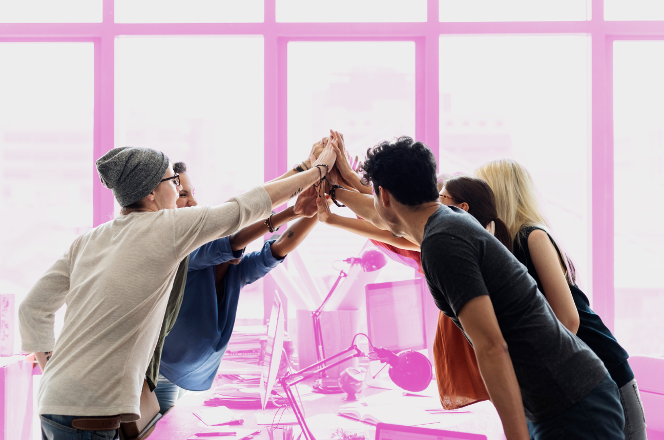 A team of co-workers high-fiving over a desk to display how positive psychology impacts recruitment marketing messaging